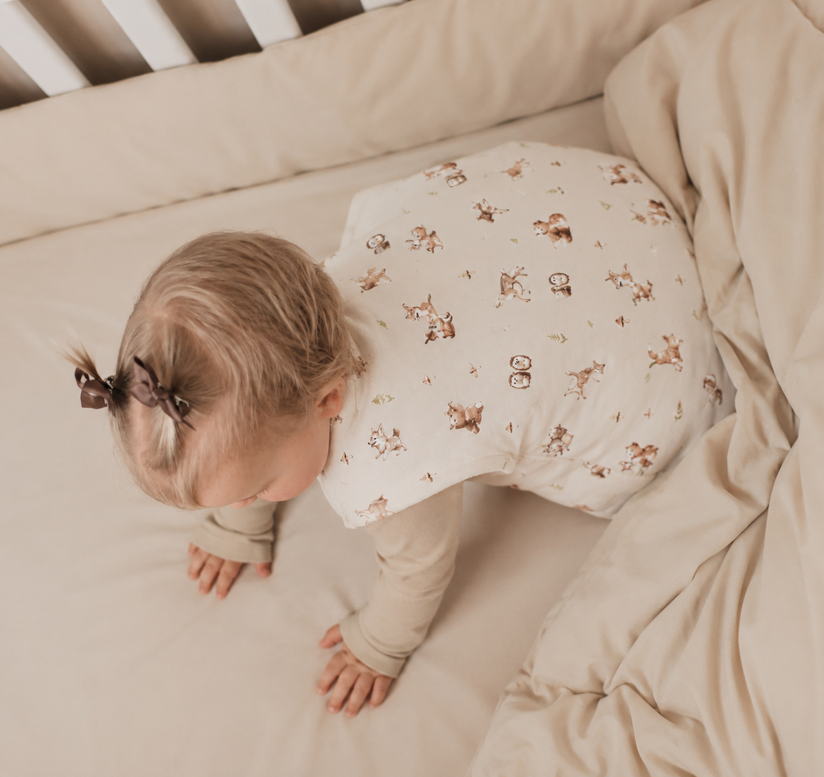 Baby kryper i spjälsäng iklädd sovpåse klassisk Skogens Vänner från ZUZU Studio – mjuk cremevit sovpåse med söta skogsdjur och naturliga jordtoner